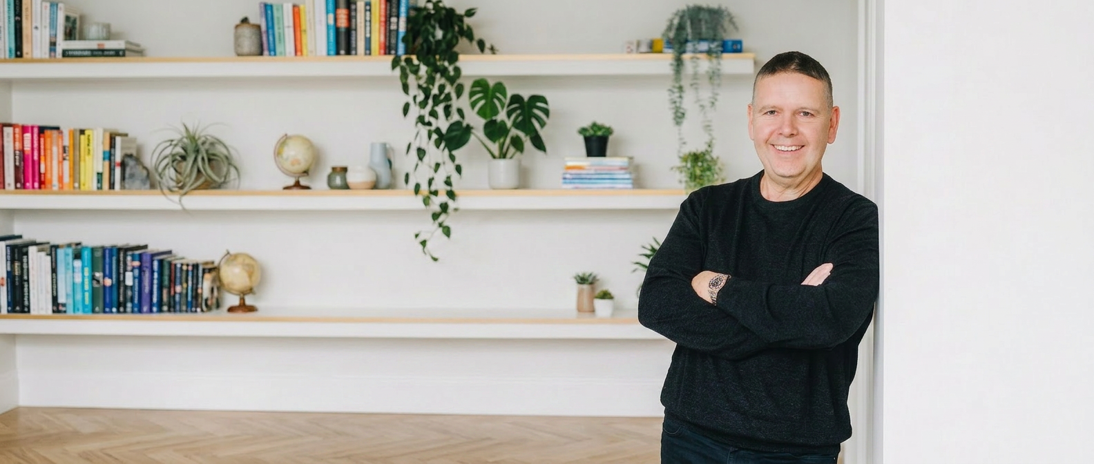 Steve Matthews smiling, arms crossed, in his studio with bookshelves